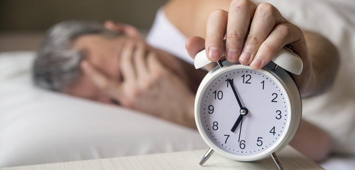 Man lying in bed turning off an alarm clock in the morning at 7a Il sonno, il nostro alleato di salute e longevità
